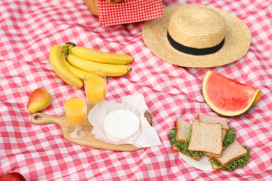 Different food, juice and hat on picnic blanket, closeup