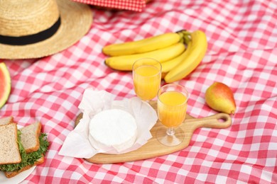 Different food, juice and hat on picnic blanket, closeup