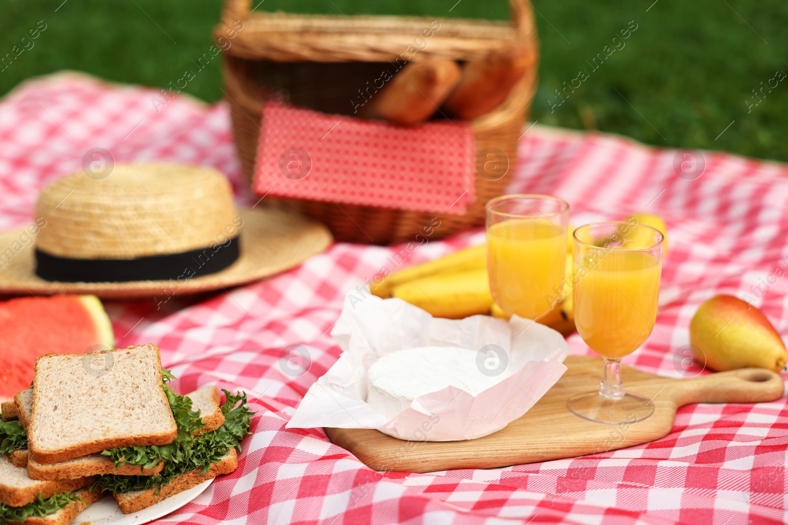 Photo of Different food, juice and hat on picnic blanket outdoors, closeup