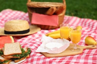 Different food, juice and hat on picnic blanket outdoors, closeup