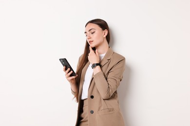 Woman in beige suit using smartphone on white background