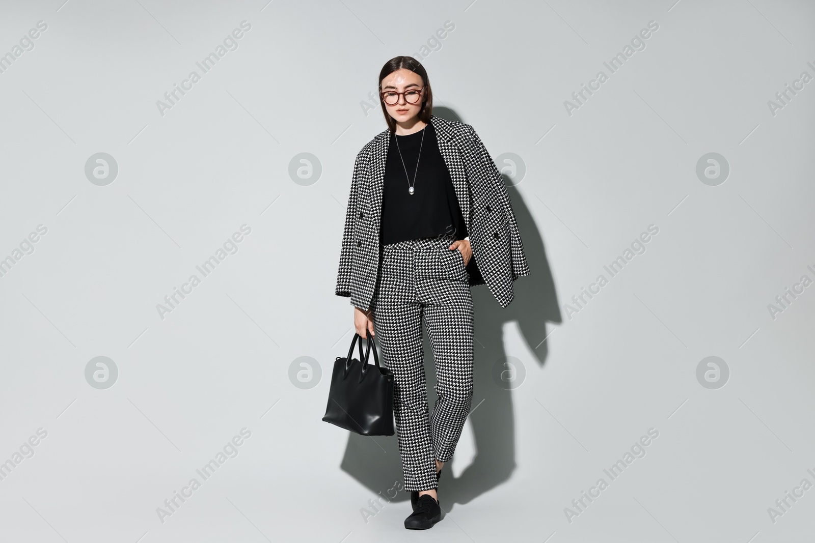 Photo of Beautiful woman in stylish suit and glasses with bag on gray background