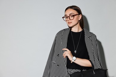 Photo of Beautiful woman in stylish suit and glasses with bag on gray background, space for text