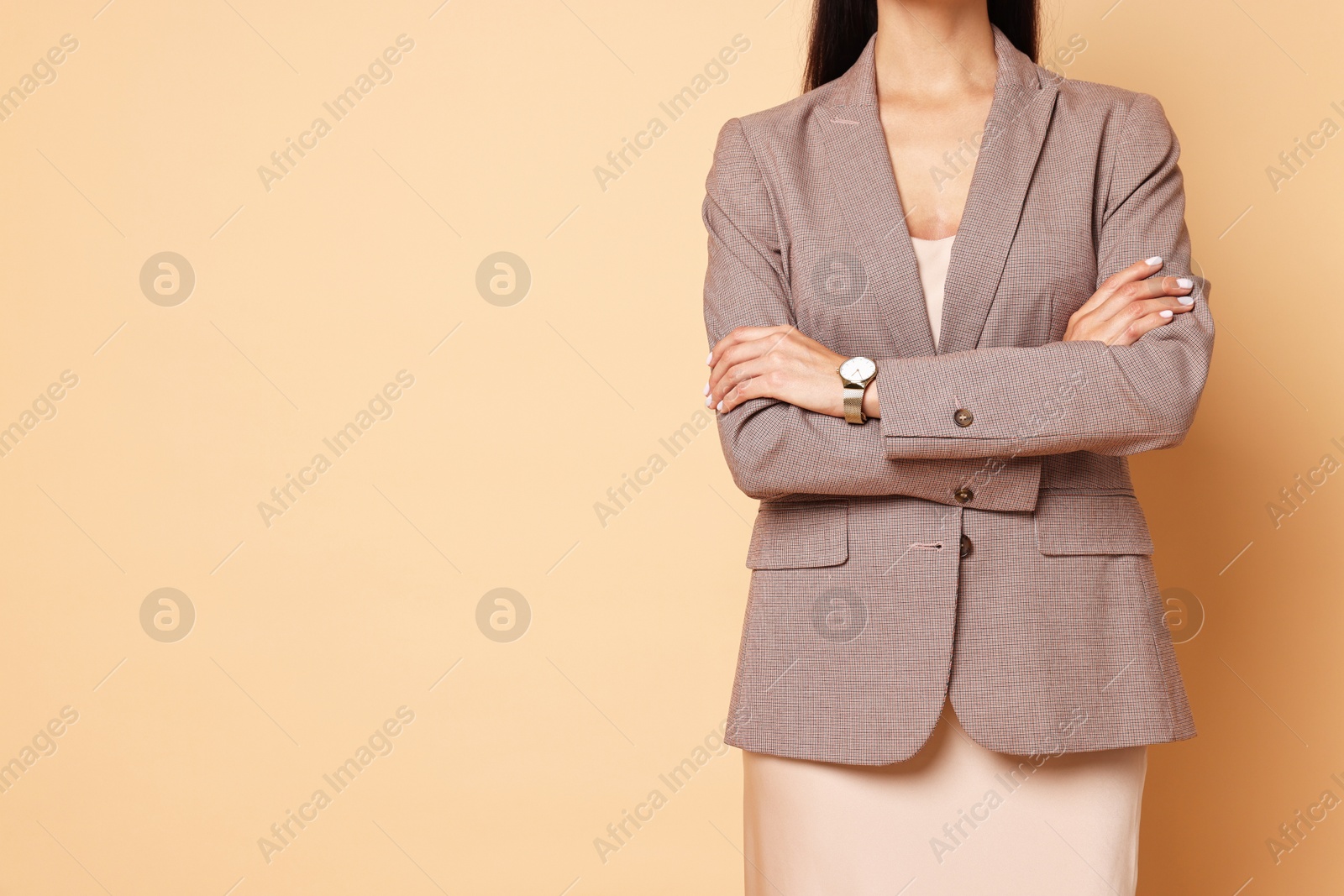 Photo of Woman in stylish jacket and beige dress on pale orange background, closeup. Space for text