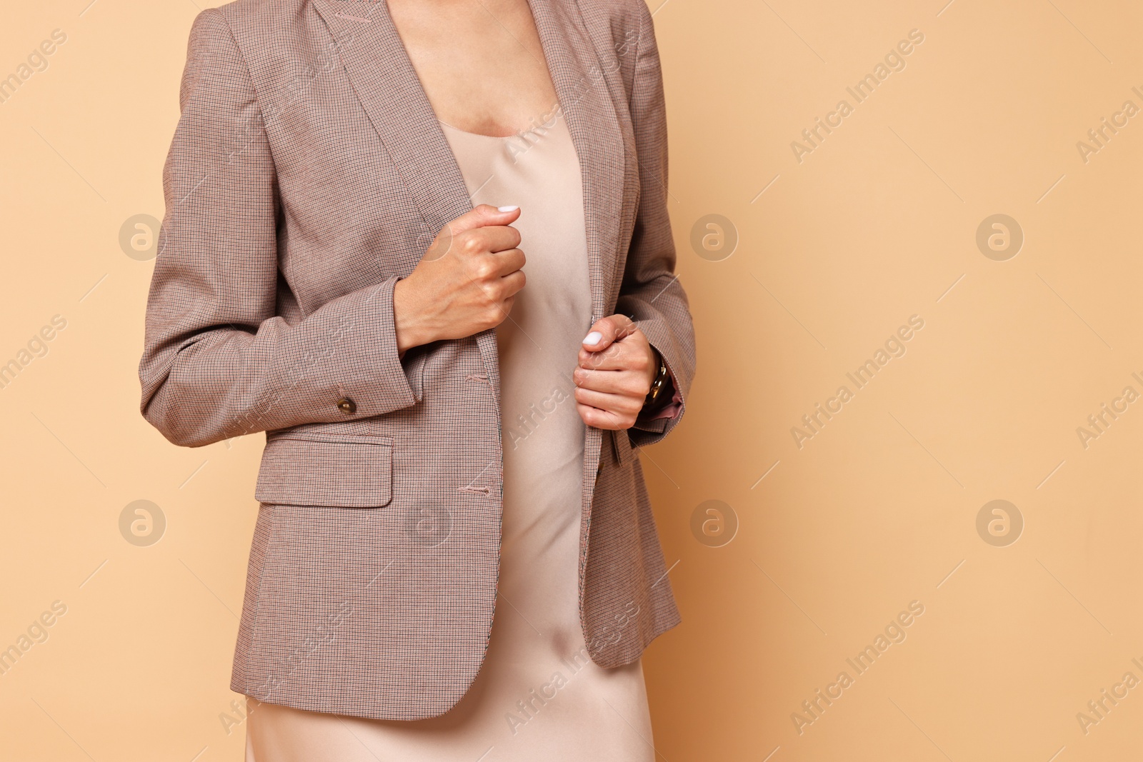 Photo of Woman in stylish jacket and beige dress on pale orange background, closeup. Space for text