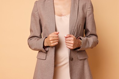 Woman in stylish jacket and beige dress on pale orange background, closeup