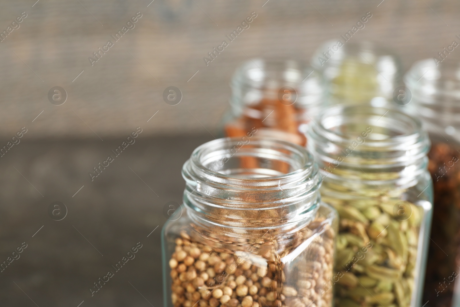 Photo of Different spices in glass jars on blurred background, closeup. Space for text