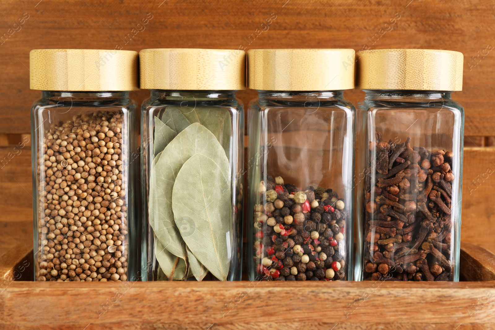 Photo of Different spices in glass jars on wooden shelf, closeup