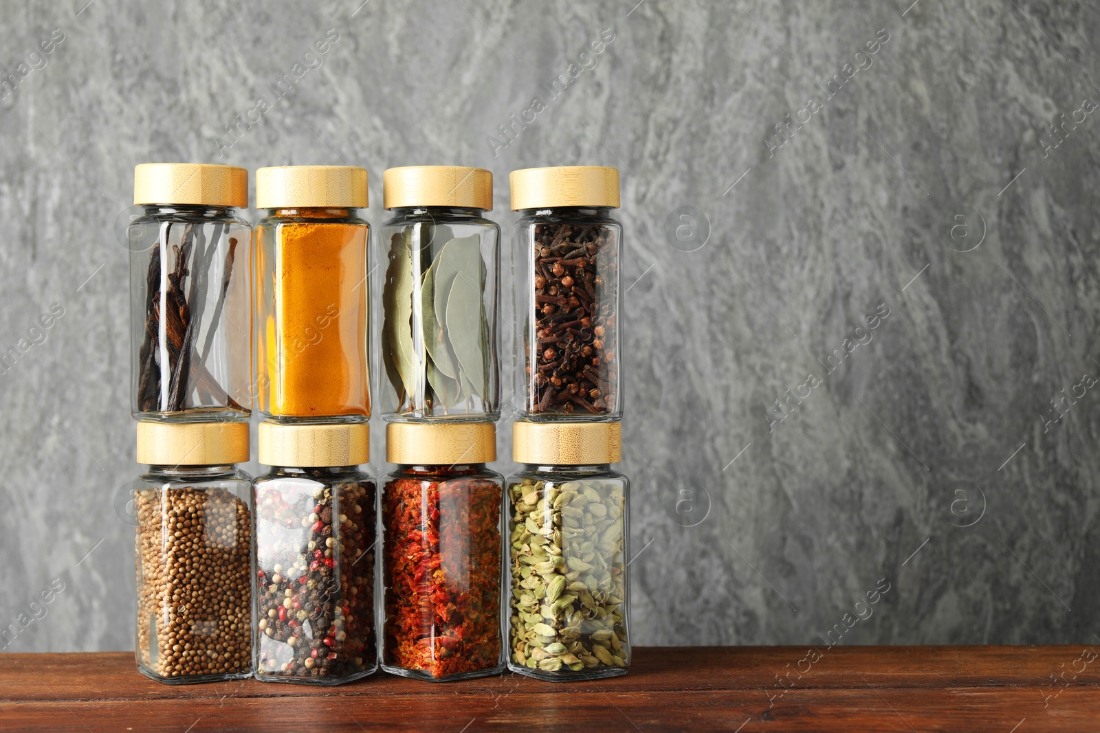 Photo of Different spices in glass jars on wooden table, space for text