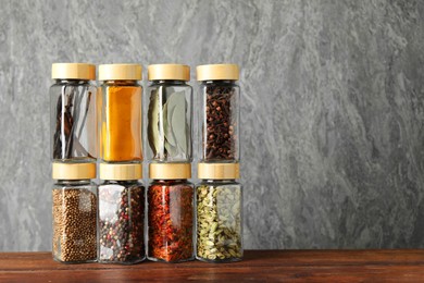 Photo of Different spices in glass jars on wooden table, space for text