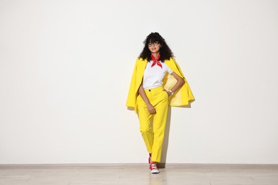 Beautiful young woman in stylish yellow suit near light wall