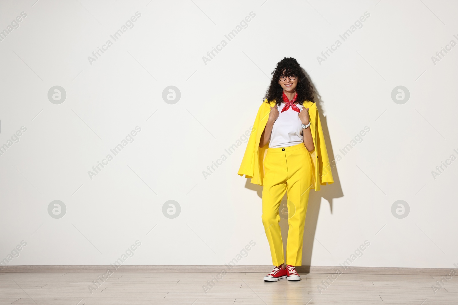 Photo of Beautiful young woman in stylish yellow suit near light wall, space for text