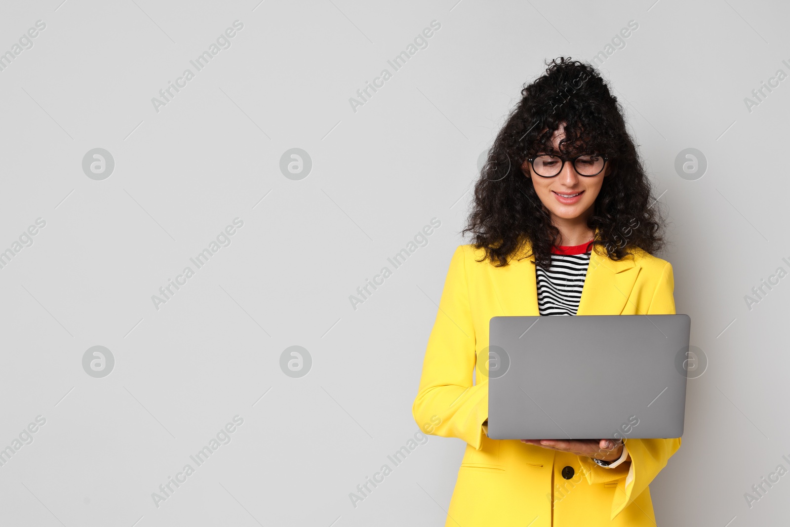 Photo of Beautiful young woman in stylish yellow suit using laptop on grey background, space for text