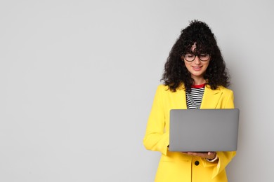 Beautiful young woman in stylish yellow suit using laptop on grey background, space for text