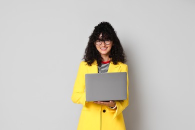 Photo of Beautiful young woman in stylish yellow suit with laptop on grey background