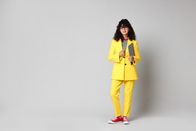 Beautiful young woman in stylish yellow suit with laptop on grey background, space for text