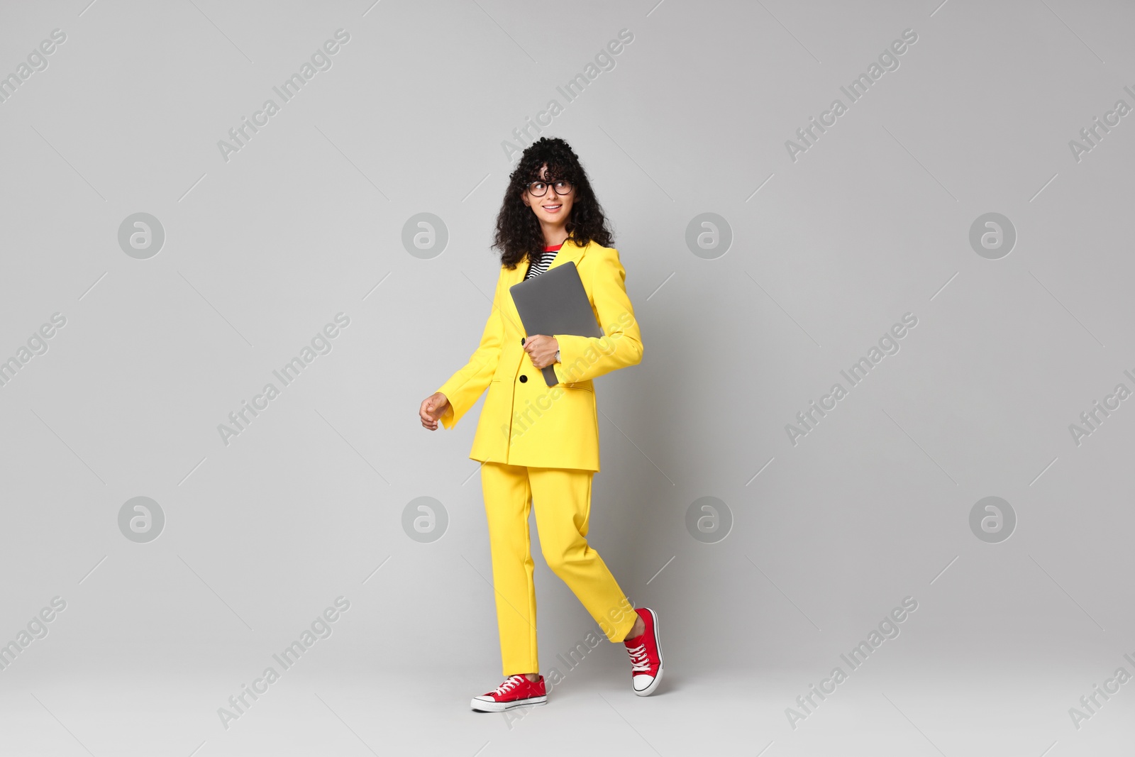 Photo of Beautiful young woman in stylish yellow suit with laptop on grey background