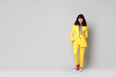 Beautiful young woman in stylish yellow suit on grey background, space for text