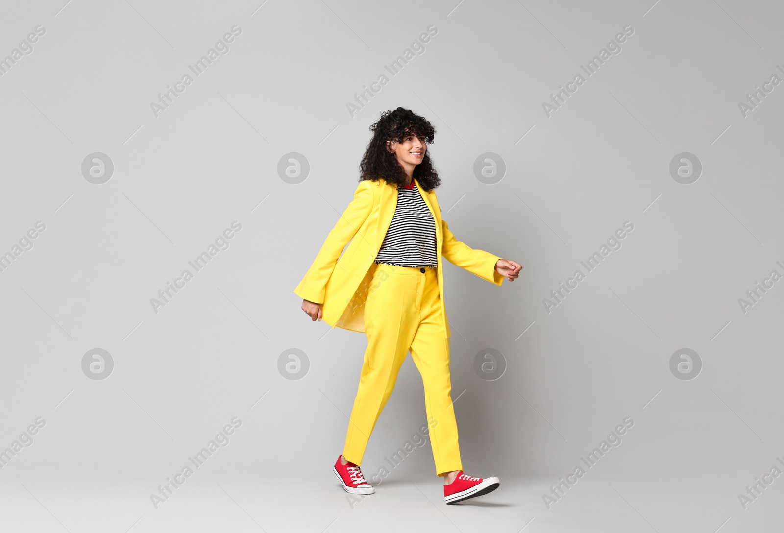 Photo of Beautiful young woman in stylish yellow suit walking on grey background