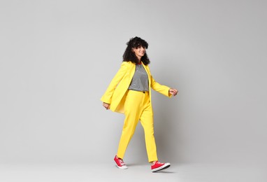 Beautiful young woman in stylish yellow suit walking on grey background