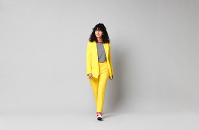 Photo of Beautiful young woman in stylish yellow suit walking on grey background