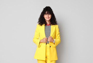 Beautiful young woman in stylish yellow suit on grey background