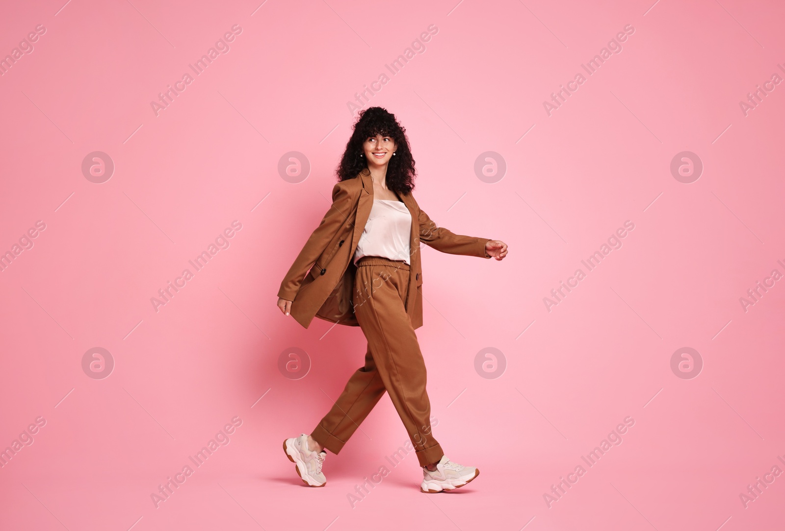 Photo of Beautiful young woman in stylish suit walking on pink background