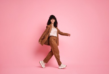 Photo of Beautiful young woman in stylish suit walking on pink background