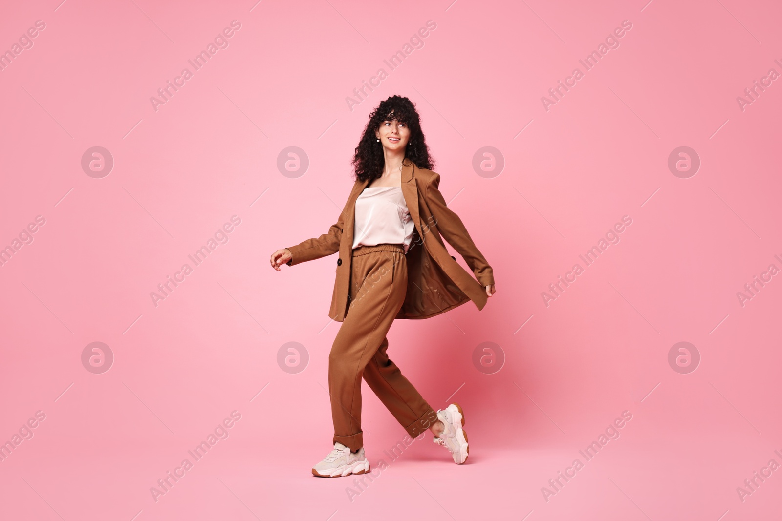 Photo of Beautiful young woman in stylish suit walking on pink background