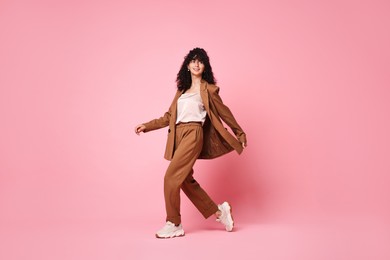 Photo of Beautiful young woman in stylish suit walking on pink background