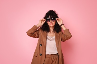 Photo of Beautiful young woman in stylish suit and sunglasses on pink background