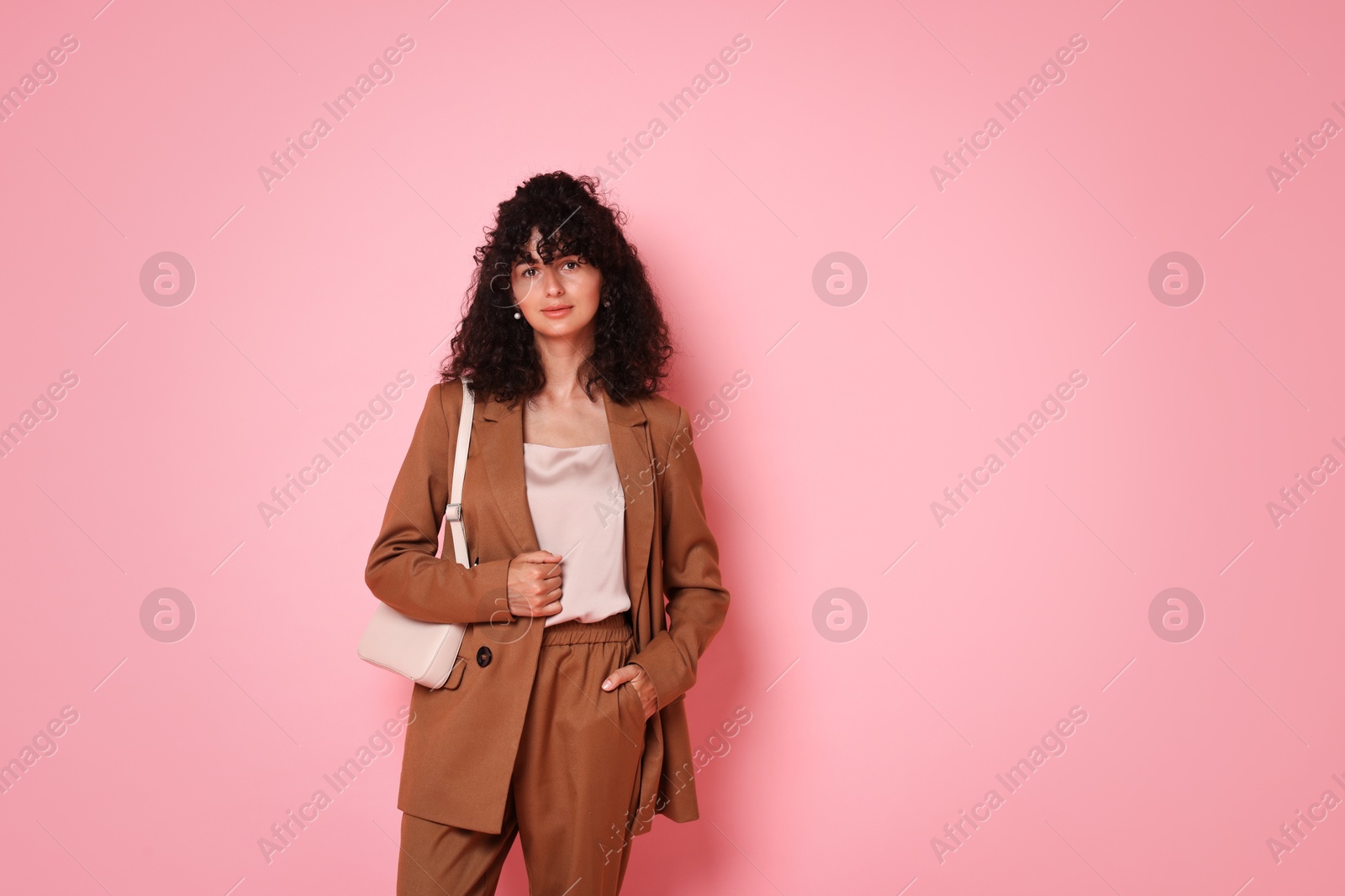 Photo of Beautiful young woman in stylish suit with bag on pink background, space for text