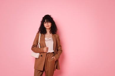 Photo of Beautiful young woman in stylish suit with bag on pink background, space for text