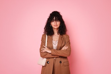 Beautiful young woman in stylish suit with bag on pink background