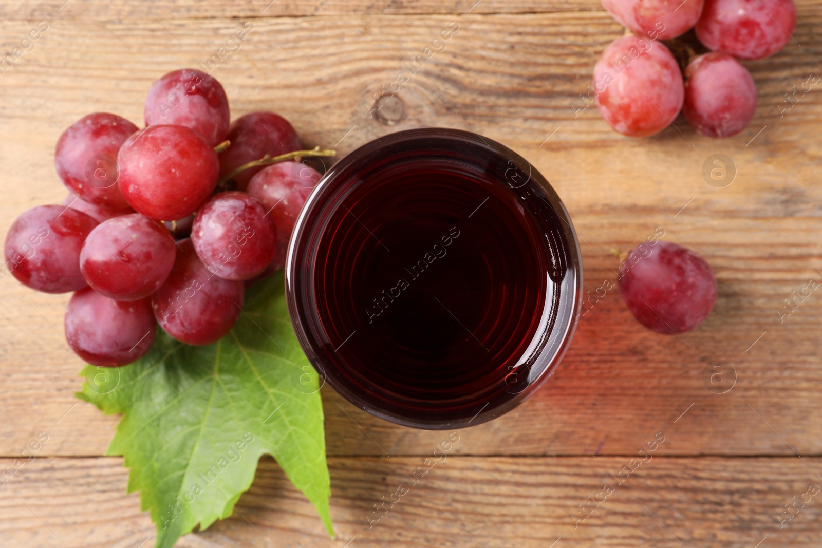 Photo of Tasty juice in glass, fresh grapes and leaf on wooden table, top view