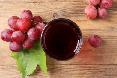 Tasty juice in glass, fresh grapes and leaf on wooden table, top view