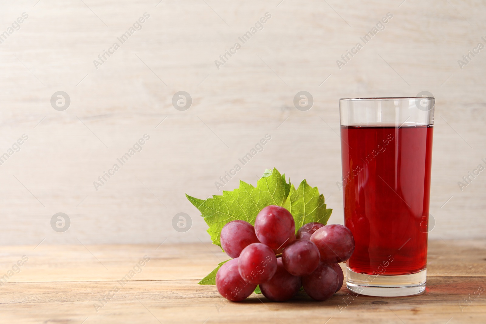 Photo of Tasty juice in glass, fresh grapes and leaf on wooden table, space for text