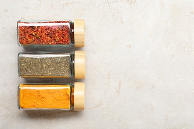 Photo of Different spices in glass jars on light grey table, top view. Space for text