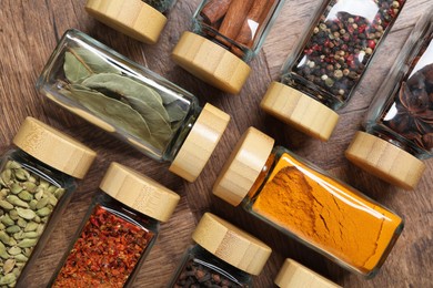 Different spices in glass jars on wooden table, flat lay