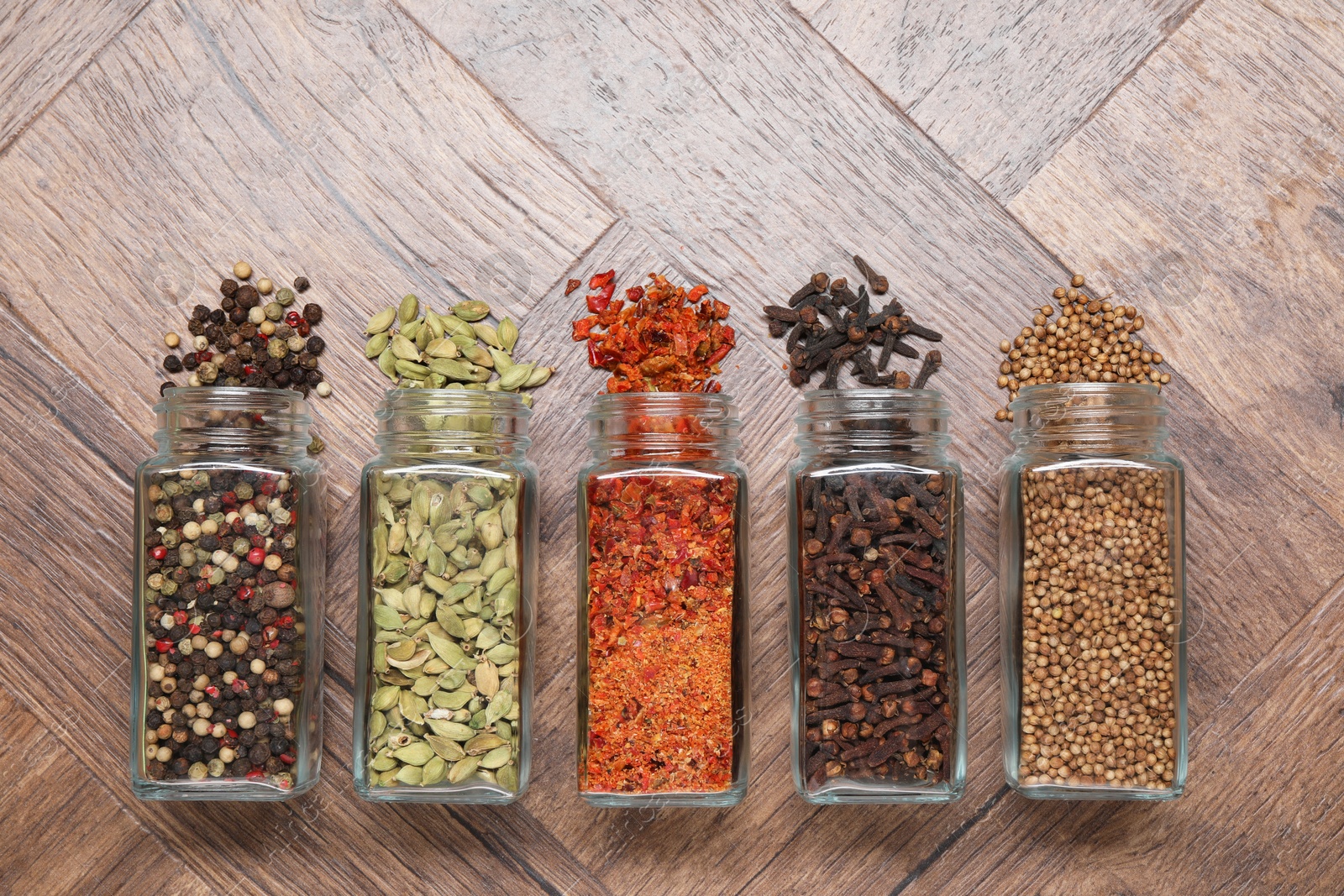 Photo of Different spices in glass jars on wooden table, flat lay