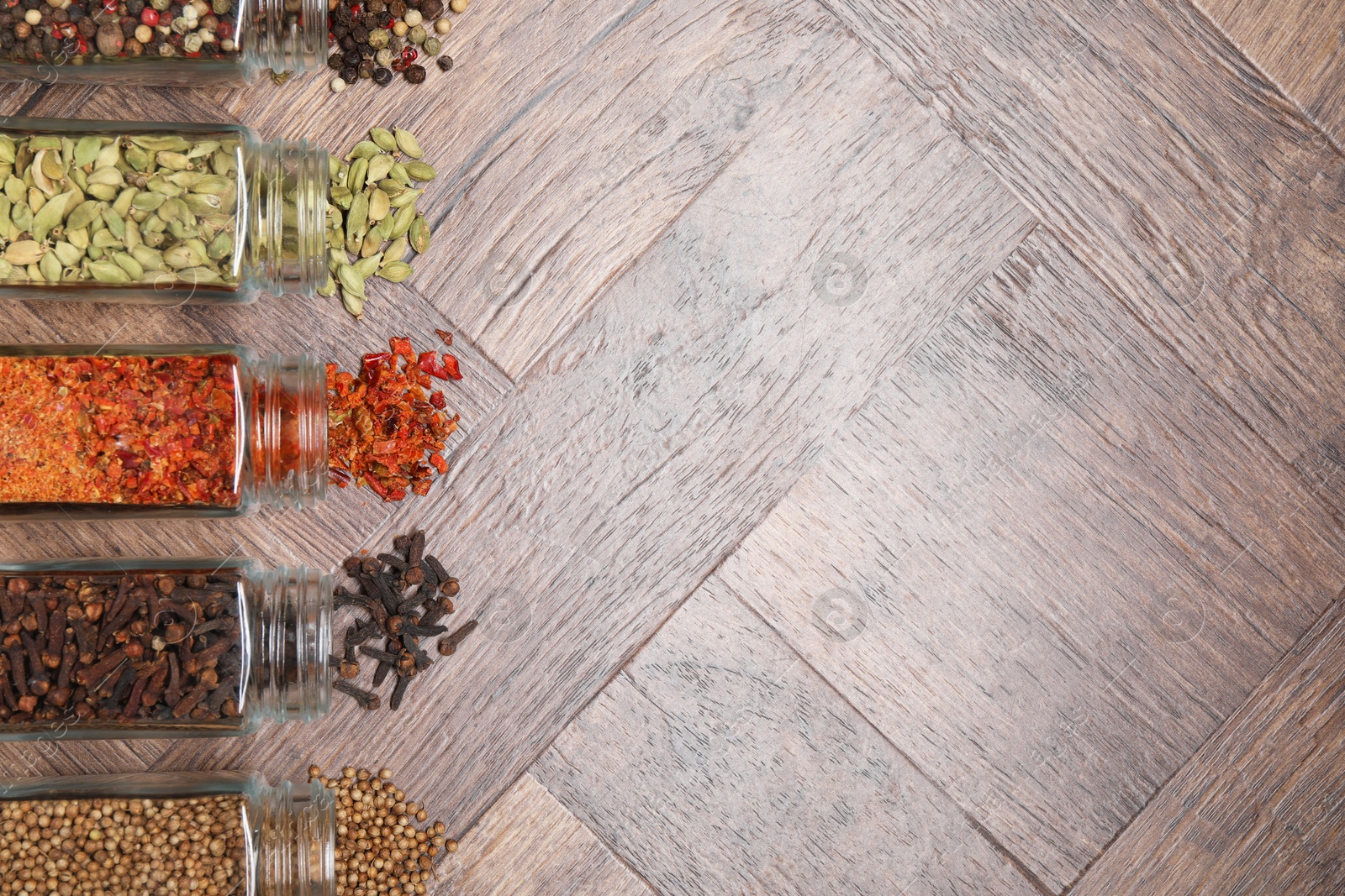 Photo of Different spices in glass jars on wooden table, flat lay. Space for text