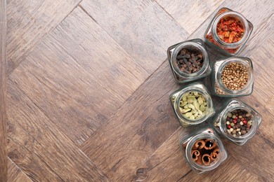 Photo of Different spices in glass jars on wooden table, flat lay. Space for text