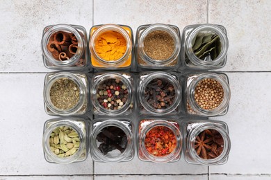 Photo of Different spices in glass jars on light tiled table, top view