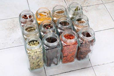 Different spices in glass jars on light tiled table