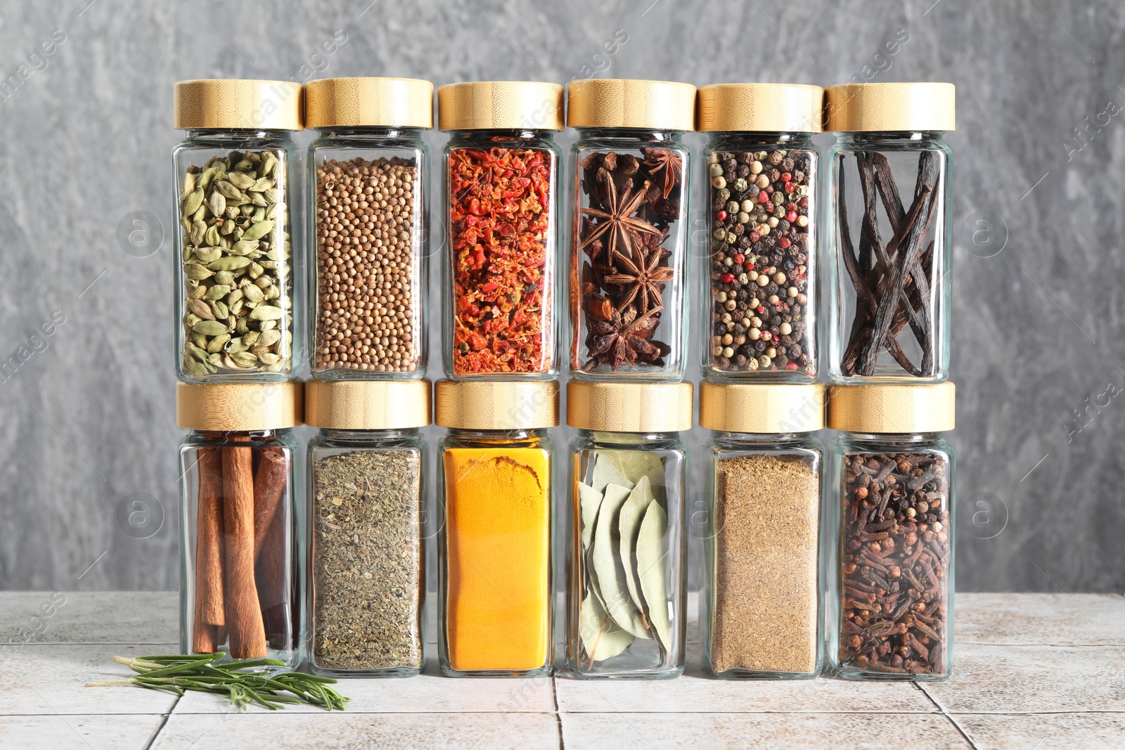 Photo of Different spices in glass jars on light tiled table