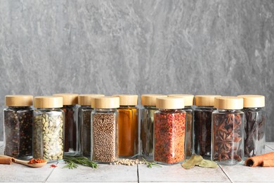 Different spices in glass jars on light tiled table, space for text