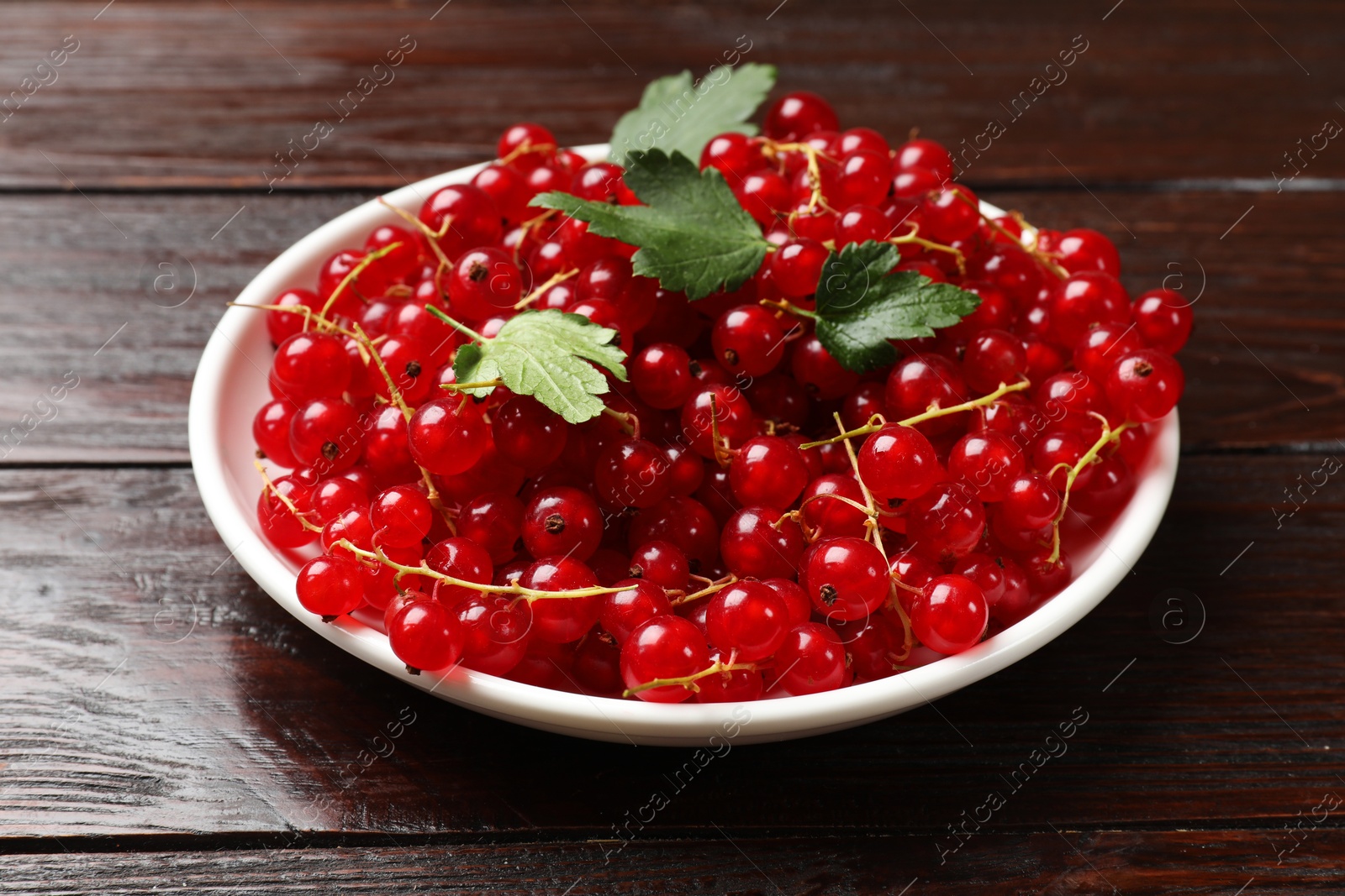 Photo of Fresh red currants and leaves on wooden table, closeup