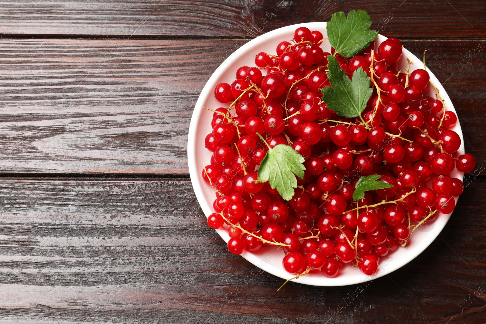 Photo of Fresh red currants and leaves on wooden table, top view. Space for text