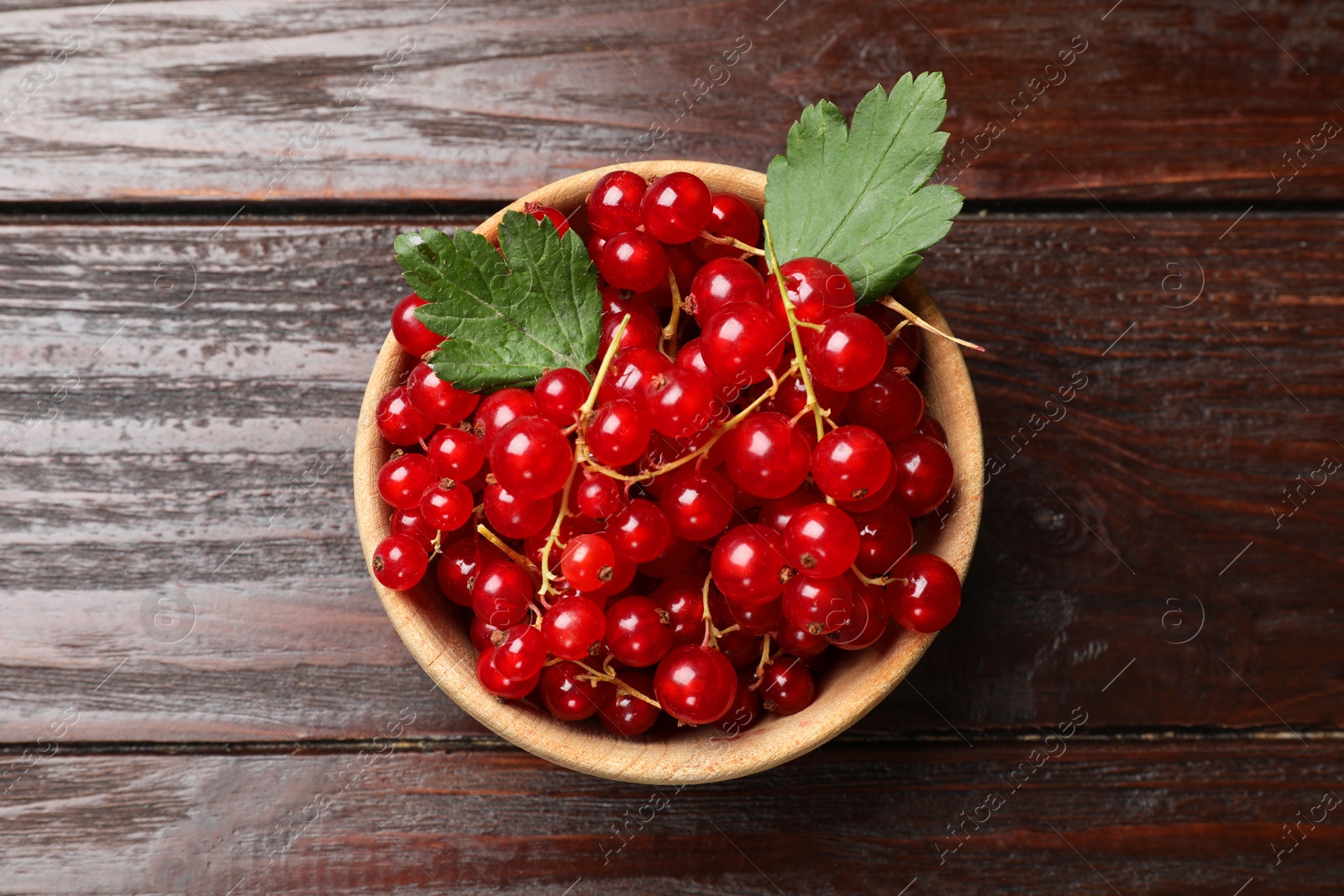 Photo of Fresh red currants in bowl and green leaves on wooden table, top view