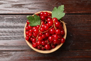 Photo of Fresh red currants in bowl and green leaves on wooden table, top view